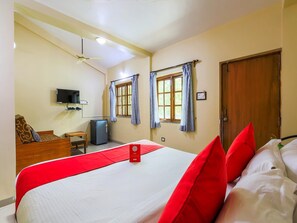 A hotel room with a bed, a television, a desk, a refrigerator, and two windows with curtains. - Classic Tanisha Guest House (Marmagao)