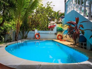 A swimming pool with a curved edge, surrounded by a white wall with a mural, and two orange lifebuoys attached to the wall. - Classic Tanisha Guest House (Marmagao)