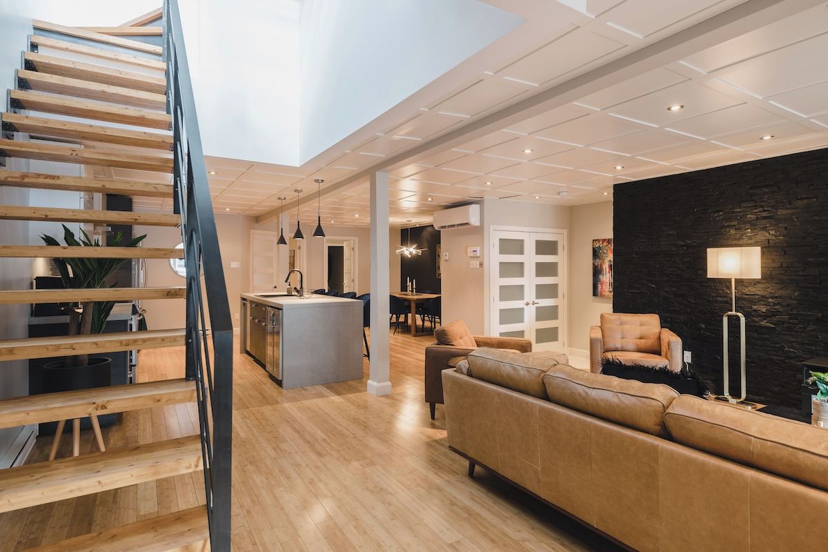 Un interior moderno con una escalera de madera, una isla central, un sofá y una pared de acento de piedra.