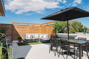 Une terrasse extérieure avec une clôture en bois, une table en verre avec des chaises et un parasol noir.