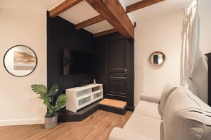 Ein Wohnzimmer mit einem weißen Sofa, einer schwarzen Tür, einem Wandfernseher und einem Blumentopf.