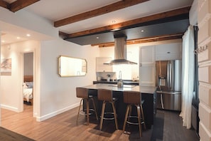 A modern kitchen with a central island, bar stools, a large stainless steel range hood, and a refrigerator. - Limoilou | 3 Bedrooms | Terrace | The 703 (Québec City)
