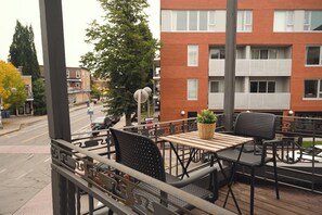An outdoor seating area with tables and chairs, a potted plant, and a view of a red brick building with balconies. - Limoilou | 3 Bedrooms | Terrace | The 703 (Québec City)