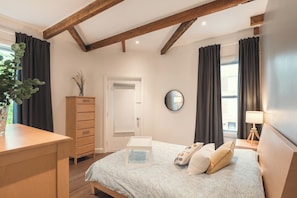 Ein Schlafzimmer mit einem Bett, einem Schminktisch, einem Spiegel und einem Fenster mit Vorhängen.