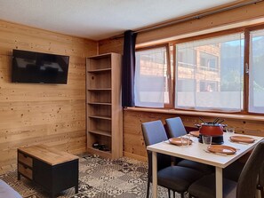 A wooden interior with a TV, a dining table set with plates and cutlery, and a window with a view of buildings. - Enchaple S58 - 4 peoples (Saint-Jean-d´Aulps)