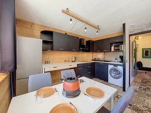 Une cuisine compacte dotée d’appareils électroménagers modernes, un coin repas avec une table dressée pour deux personnes, et un lave-linge.