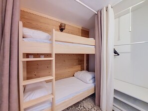 Un lit superposé avec une échelle, une étagère et une petite tablette équipée d’une prise électrique.