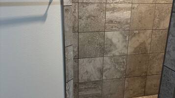 Un espace douche avec un mur et un sol carrelés, un porte-serviettes en métal et un tapis à rayures.