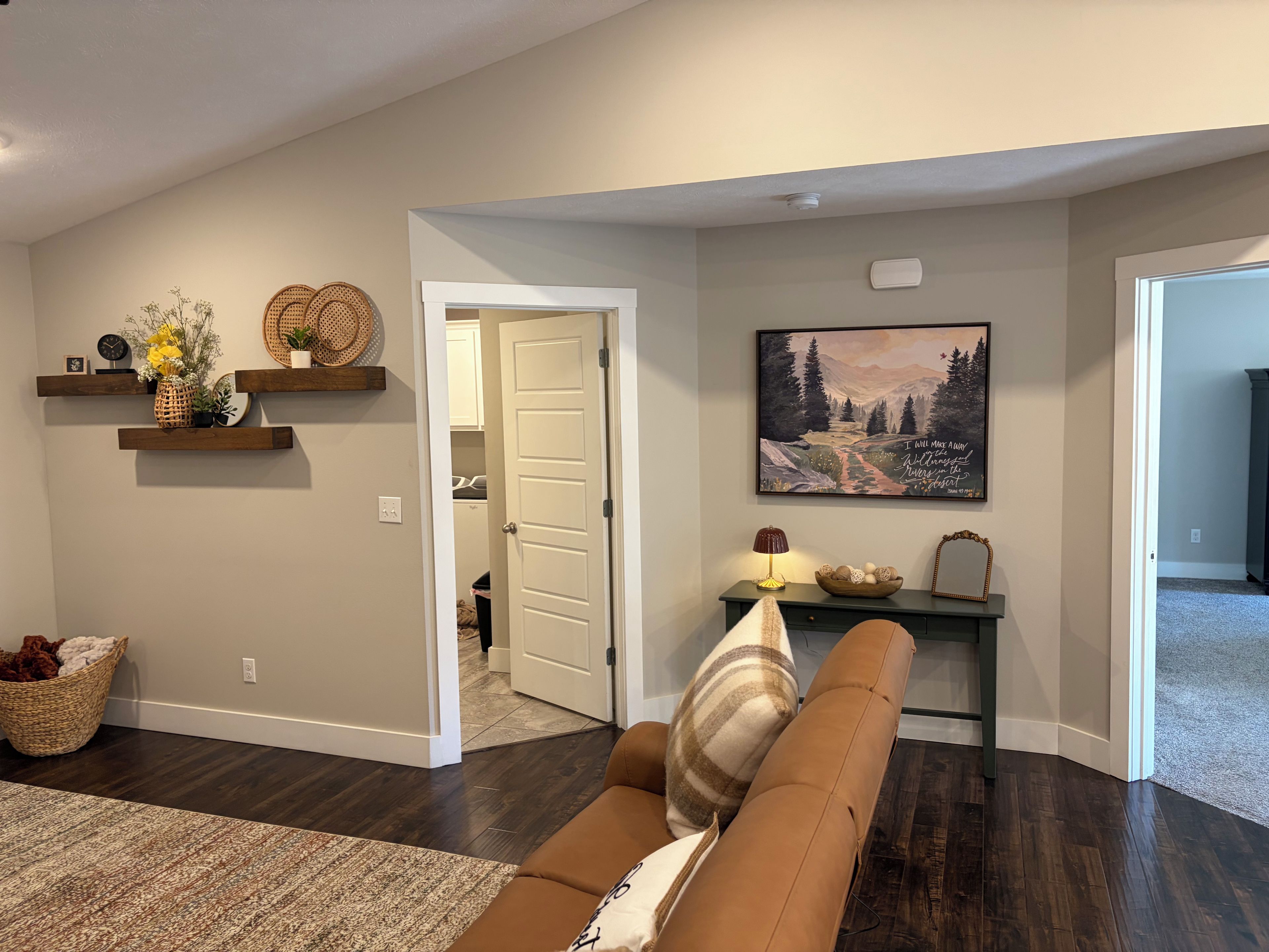Un salon avec un canapé marron, une étagère décorative fixée au mur, un tableau et une porte donnant sur une autre pièce.