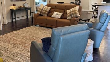 A modern living room with a brown sofa, blue recliners, a large rug, and a ceiling fan.
