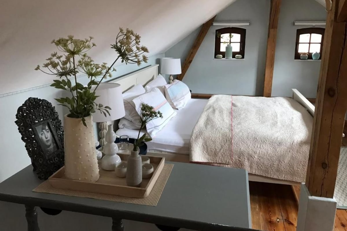 Quarto com cama, mesa de cabeceira, abajur e objetos decorativos.