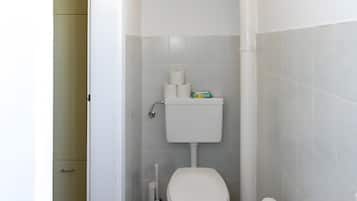 A small bathroom with a toilet, a cabinet above it, and a shower area.