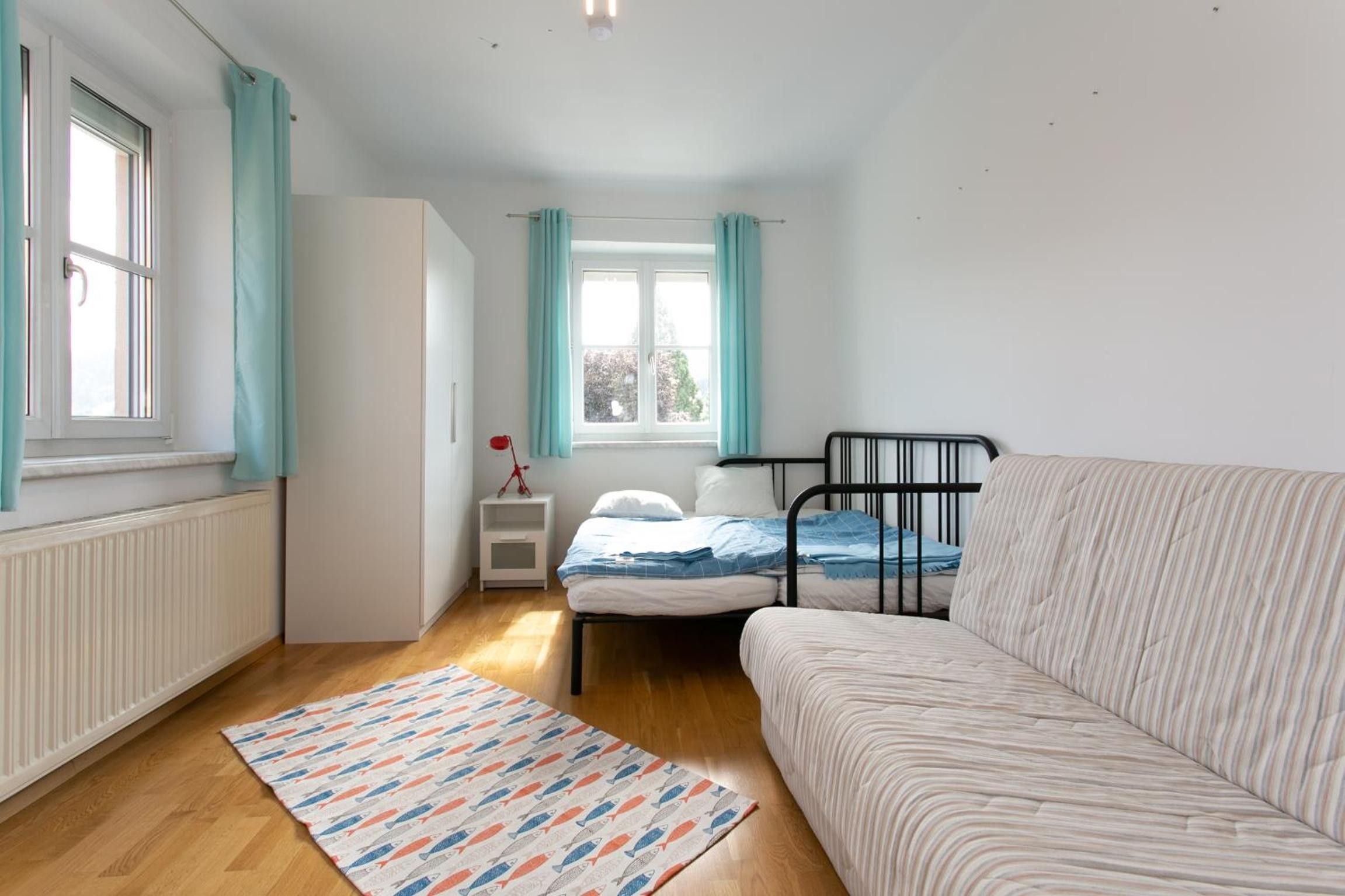 A bedroom with a bed, a nightstand, a window, and a radiator.