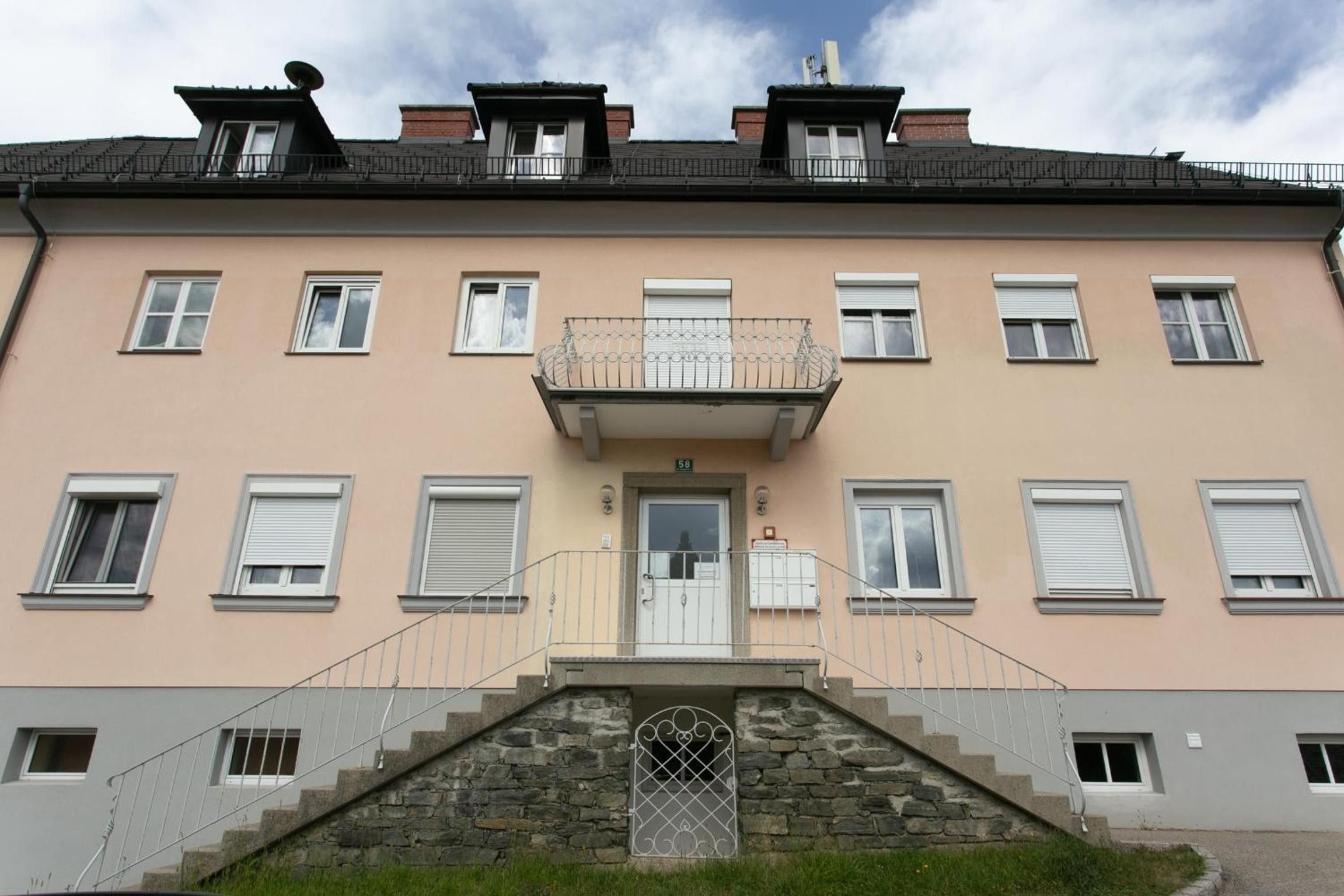 Un immeuble à plusieurs étages doté d’une entrée centrale, d’un escalier en pierre menant à l’entrée et d’un balcon au deuxième étage.