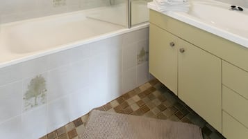 A modern bathroom with a glass-enclosed shower, a white bathtub, and a vanity with a mirror.