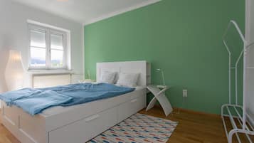 Un dormitorio con cama, ventana, radiador, mesita de noche y pared verde.