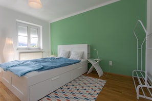 A bedroom with a bed, a window, a radiator, a bedside table, and a green wall. - Apartment 'Familienglück in Der Weststeiermark' with Wi-Fi (Sankt Oswald ob Eibiswald)