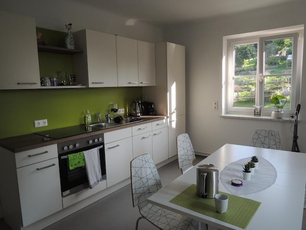 A modern kitchen with white cabinets, a green backsplash, and a dining area with a white table and chairs. - Apartment 'Familienglück in Der Weststeiermark' with Wi-Fi (Sankt Oswald ob Eibiswald)