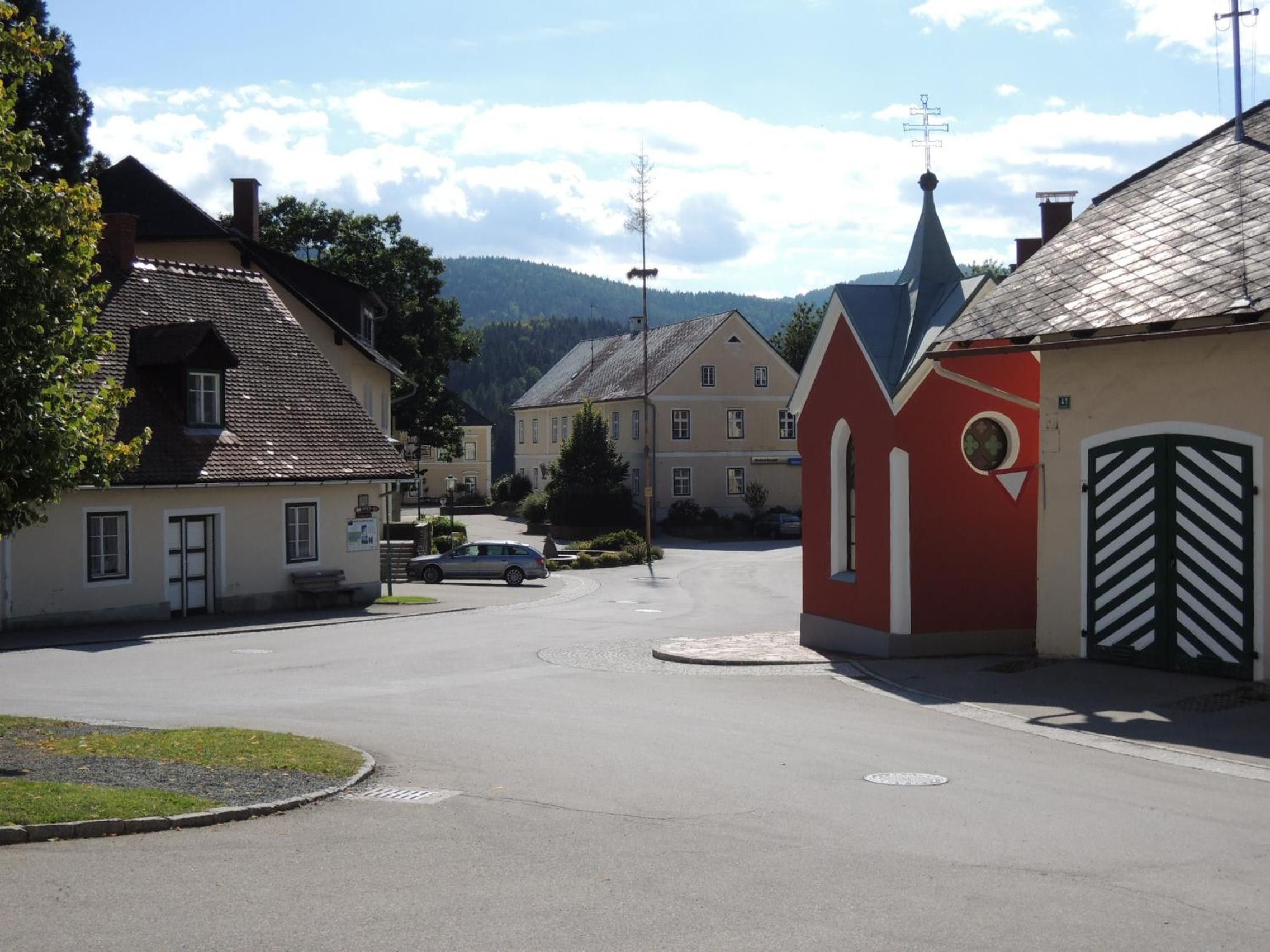A quiet street with traditional buildings, a church steeple, and a car parked on the side.