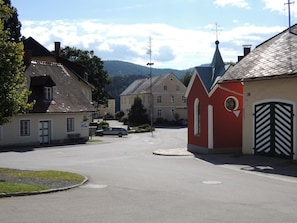 A quiet street with traditional buildings, a church steeple, and a car parked on the side. - Apartment 'Familienglück in Der Weststeiermark' with Wi-Fi (Sankt Oswald ob Eibiswald)