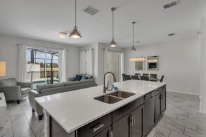 A modern kitchen with a large island, pendant lighting, and a view to the outdoors. - Oasis Villa Retreat at Champions Gate (Davenport)