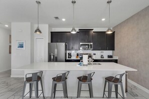 A modern kitchen with a large island, bar stools, stainless steel appliances, and pendant lighting. - Oasis Villa Retreat at Champions Gate (Davenport)