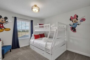 Et værelse med køjeseng, et vindue med gardiner og vægdekorationer af Mickey og Minnie Mouse.