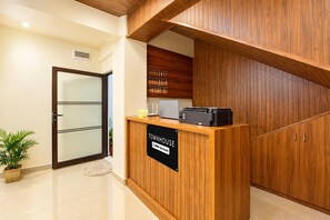 A reception desk with a sign indicating it is an OYO Service center, a reception area with a wooden panel wall, a door with a frosted glass panel, and a potted plant.