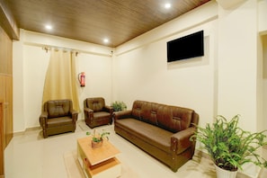 Una sala de estar con un sofá, dos sillones, una mesa de centro y un televisor de pantalla plana montado en la pared.