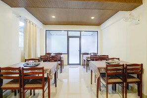 A dining area with multiple tables and chairs, a wooden ceiling, and a large window with frosted glass. - Classic The Polo Continental (Shillong)