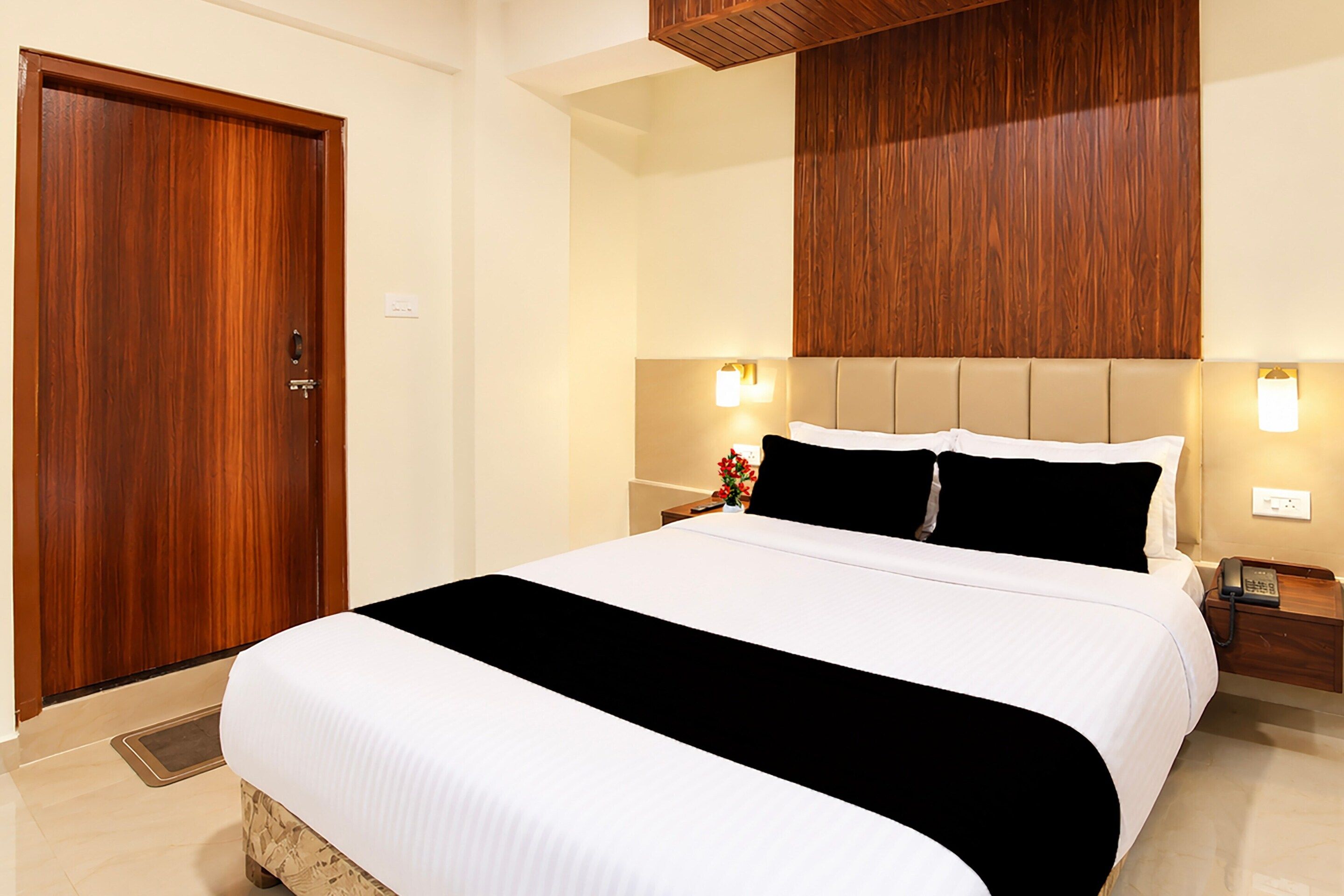 A hotel room with a large bed, a wooden door, and a wall-mounted light fixture.
