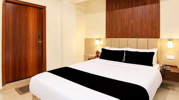 A hotel room with a large bed, a wooden door, and a wall-mounted light fixture.