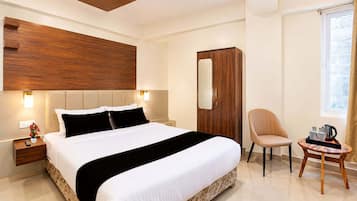 A modern hotel room with a large bed, a wooden headboard, a wardrobe, a chair, and a small table with a tray.