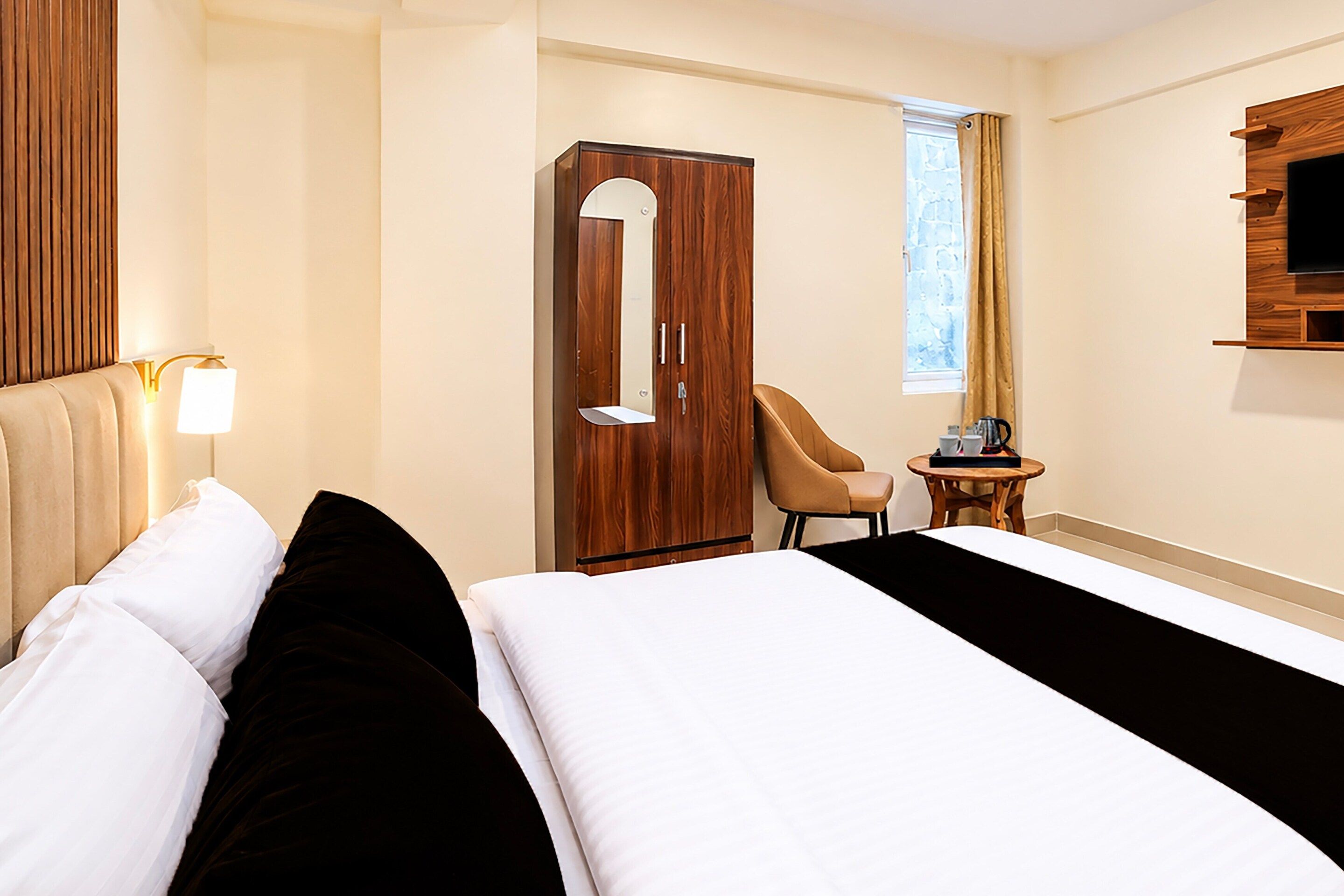 Habitación de hotel con cama, armario, silla, mesita y televisor montado en la pared.