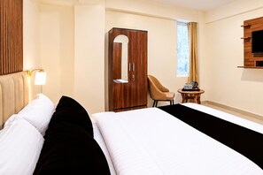 A hotel room with a bed, a wardrobe, a chair, a small table, and a television mounted on the wall.