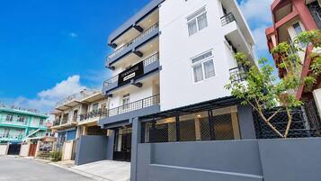Un edificio residencial de varios pisos con balcones, entrada protegida por una reja y cielo despejado.