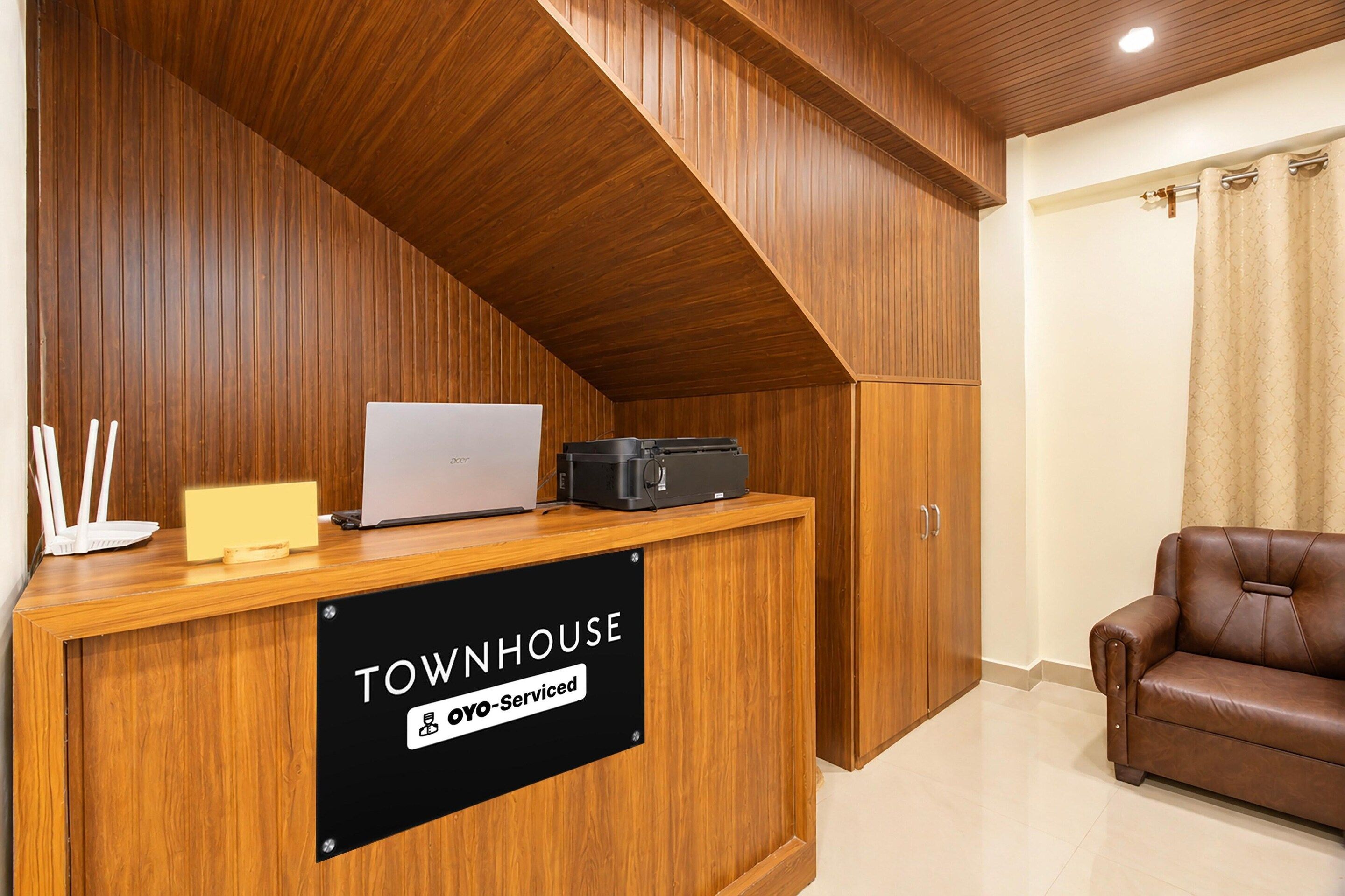 Una mesa de recepción con una computadora portátil, una impresora y un cartel que indica 'TOWNHOUSE & OYO-Serviced'.