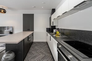 Uma cozinha moderna com ilha central, armários pretos e piso em padrão herringbone.