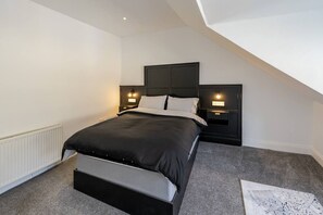 A modern bedroom with a bed, bedside tables, and a television mounted on the wall. - Newmarket Suites 21 in Ayr (South Ayrshire)