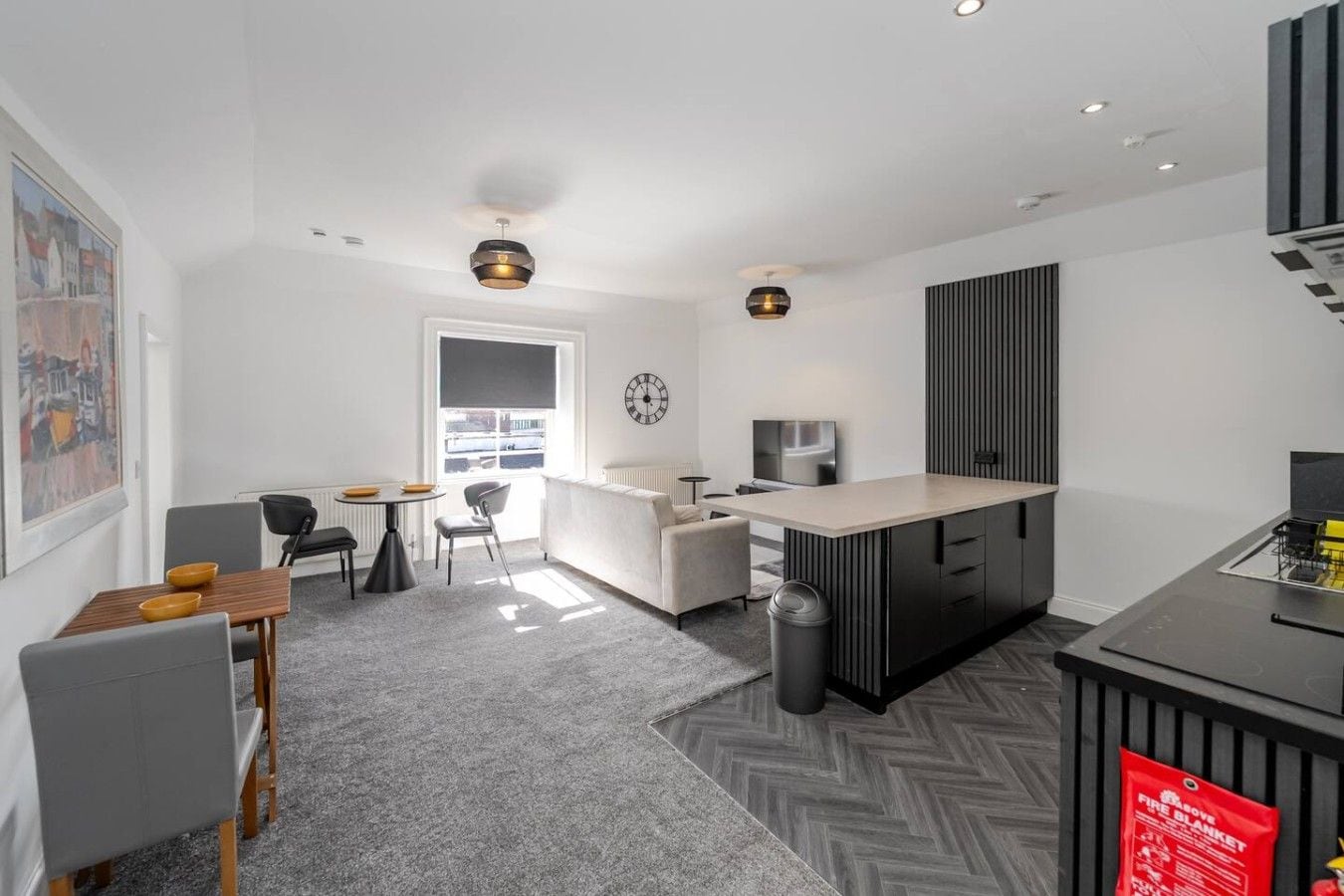 A modern kitchen with a central island, a dining area with a table and chairs, and a living space with a sofa and a television.