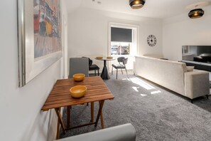 A modern living room with a sofa, a dining table with two bowls, a TV, and a large window. - Newmarket Suites 21 in Ayr (South Ayrshire)