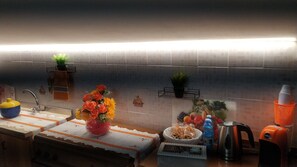 A kitchen with a tiled backsplash, a sink, a stove, a countertop with a vase of flowers, a kettle, a water bottle, and a coffee maker.