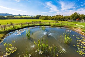 A pond with a wooden fence, surrounded by green fields and trees. - Sunken Hot Tub Lodge · Sleeps 4 · Garden Views in Bonvilston, Vale of Glamorgan (Bonvilston)