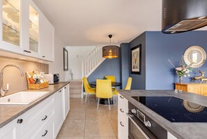A modern kitchen with white cabinets, a black stove, and a yellow dining table with chairs. - Sunken Hot Tub Lodge · Sleeps 4 · Garden Views in Bonvilston, Vale of Glamorgan (Bonvilston)