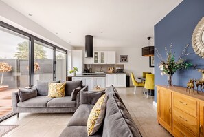 Uma sala de estar moderna com um sofá seccional cinza, um armário de madeira e uma área de jantar com cadeiras amarelas.