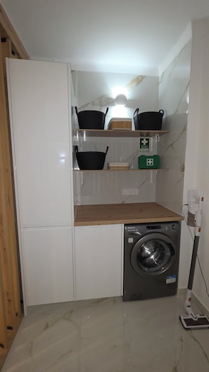 A compact laundry area with a washing machine, shelves with baskets, and a first aid kit. - Modern Apartment with Ocean View Near Downtown in a Hotel Complex (Albufeira)
