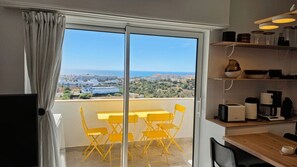 A balcony with a table and chairs, a kitchen area with appliances, and a view of a coastal town. - Modern Apartment with Ocean View Near Downtown in a Hotel Complex (Albufeira)