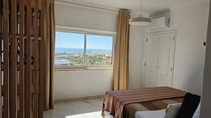 A bedroom with a large window, a bed, a wardrobe, and a hanging light fixture. - Modern Apartment with Ocean View Near Downtown in a Hotel Complex (Albufeira)