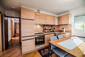 A compact kitchen with wooden cabinetry, a built-in oven, and a dining area with a table and chairs. - 3 Bedroom Apartment TI&JAZ (Brežice)