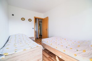 Ein Zimmer mit zwei Einzelbetten, Holzboden, weißer Wand und einer Tür zu einem anderen Raum.